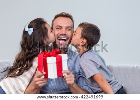 Father holding a gift and receiving kisses from son and daughter