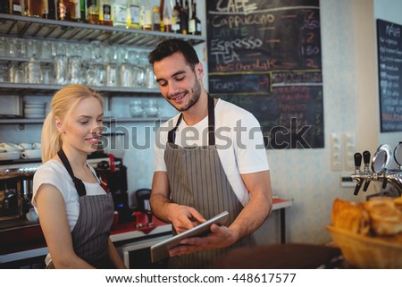 Happy co-workers using digital tablet while standing in cafe