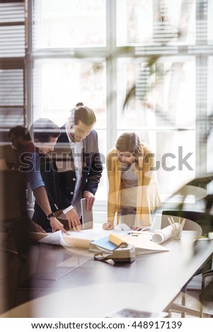Business people with digital tablet and blueprint on table seen through glass