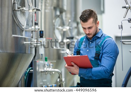 Attentive maintainance worker writing on clipboard at brewery