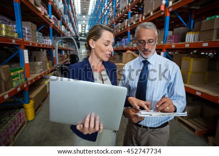 Businessmen using laptop and writing on paper in warehouse