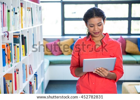 Young teacher using digital tablet at library in school