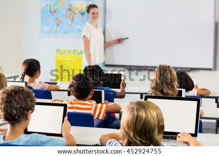 Schoolchildren using digital tablets against female teacher teaching them in classroom