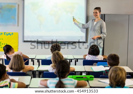 Female teacher teaching schoolchildren using projector screen in classroom
