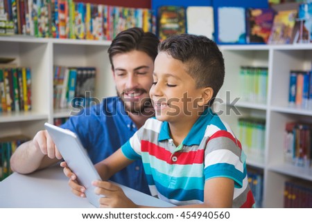 Teacher and school kid using digital table in library at school