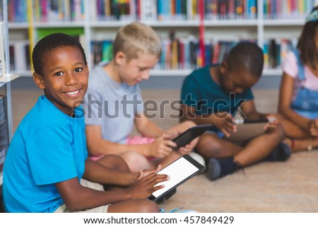 School kids sitting on floor using digital tablet in library at elementary school