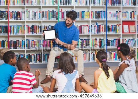 Teacher teaching kids on digital tablet in library at elementary school