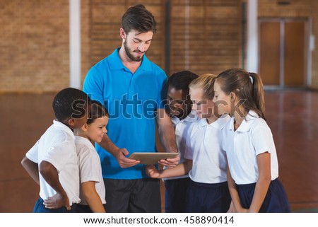 Sports teacher and school kids using digital tablet in basketball court at school gym