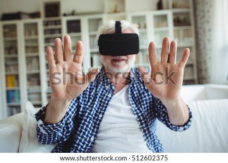 Senior man wearing virtual reality headset in living room at home