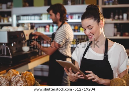 Smiling waitress standing at counter using digital tablet in cafe