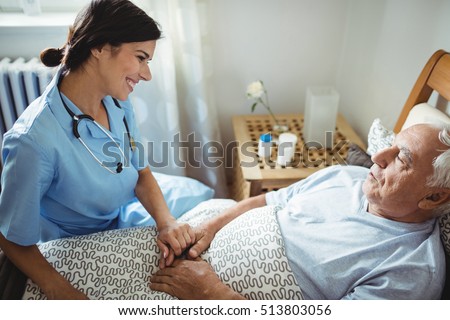 Nurse holding hands of senior man in bedroom