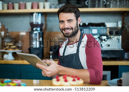 Portrait of smiling waiter using digital tablet at counter in cafe