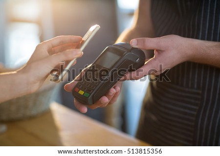 Mid-section of woman paying bill through smartphone using NFC technology in cafe