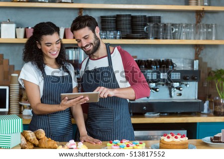 Smiling waiter and waitress using digital tablet at counter in cafÃ©