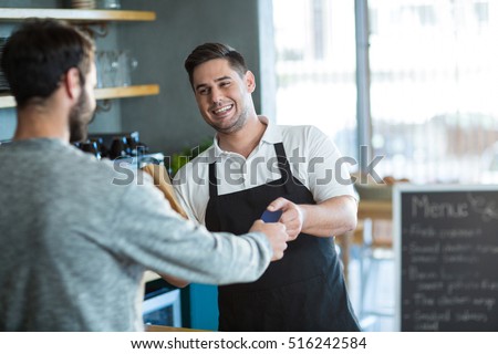 Smiling waiter giving bread to customer at counter in cafe