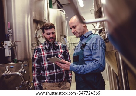 Low angle view of worker and owner discussing over digital tablet at brewery