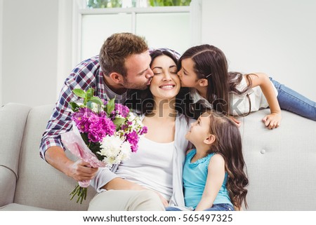 Father and daughter kissing mother sitting on sofa at home