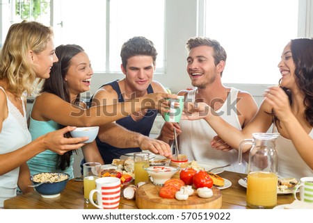 Cheerful young male and female friends having breakfast at table in house