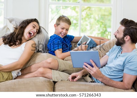 Parents and son sitting on sofa and using digital tablet at home