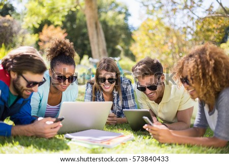 Group of friends using laptop, mobile phone and digital tablet in park