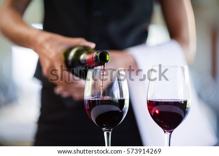 Mid section of waitress pouring red wine in a glass in restaurant