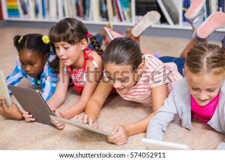Kids lying on floor using digital tablet in library