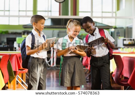 Smiling school kids using digital tablet in school cafeteria