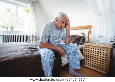 Frustrated senior man sitting on bed in bedroom