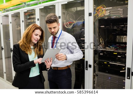 Technicians using digital tablet while analyzing server in server room