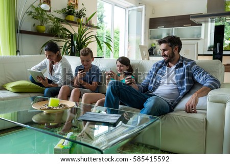 Family using laptop and mobile phone in living room at home