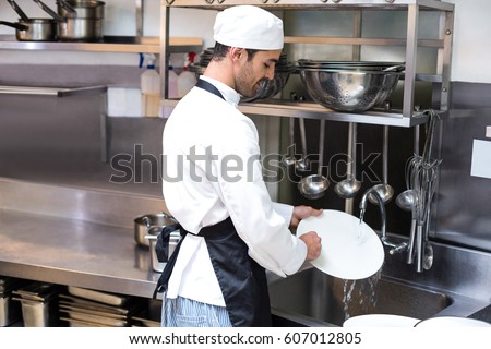 Handsome employee doing dishes in commercial kitchen