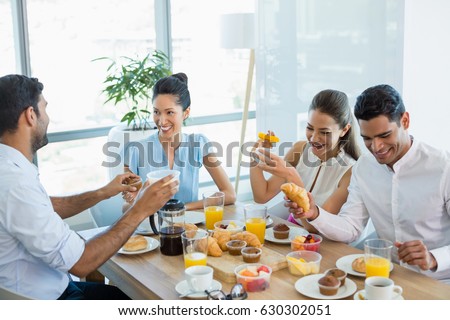 Business colleagues interacting with each other while having breakfast in office cafeteria