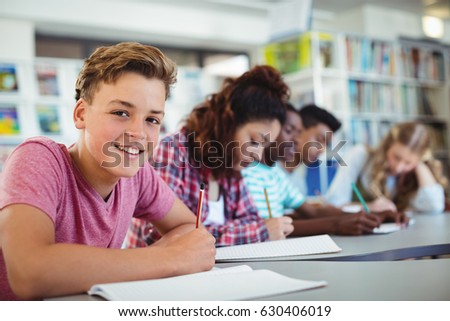 Portrait of happy schoolboy studying in library at school