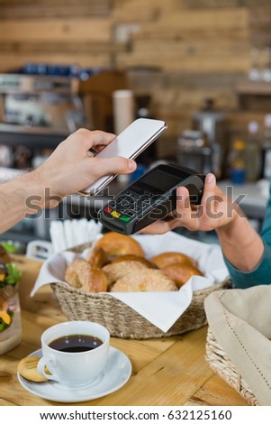 Customer paying bill through smartphone using NFC technology at counter in cafe