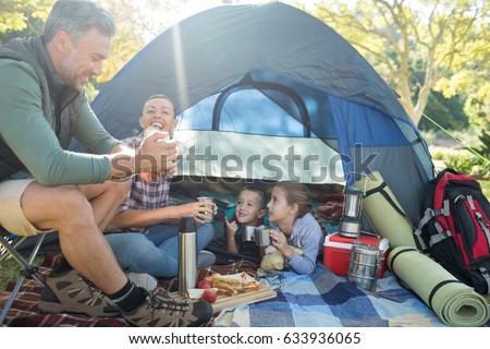 Family interacting while having snacks outside the tent at campsite