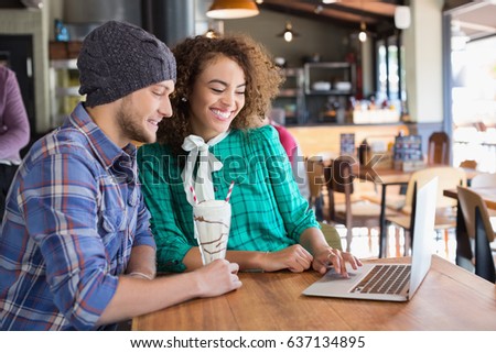 Happy friends using laptop while sitting at table in restaurant