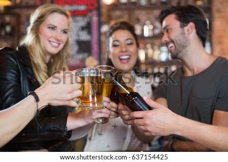 Happy friends toasting beer mugs and bottles in bar