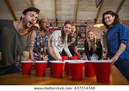 Young friends playing beer pong game on table in bar