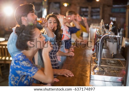 Friends drinking vodka shorts by counter in bar