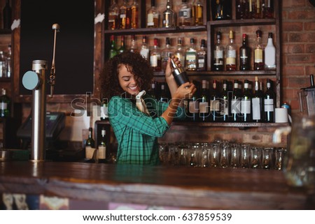 Female bartender mixing a cocktail drink in cocktail shaker at counter