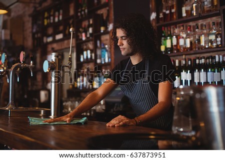 Young waiter cleaning a counter in pub