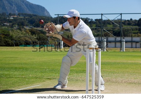 Full length of wicketkeeper catching cricket ball behind stumps on field during sunny day