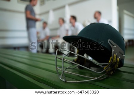 Close up of cricket helmet on table against team in locker room