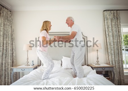 Happy senior couple dancing on bed in bedroom