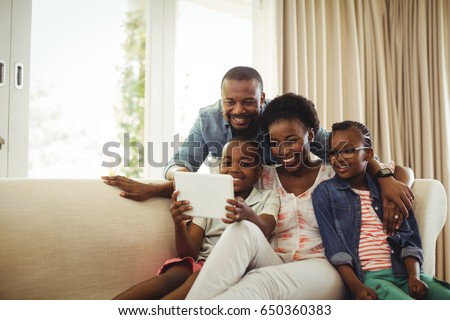 Parents and son using digital tablet on sofa in living room at home