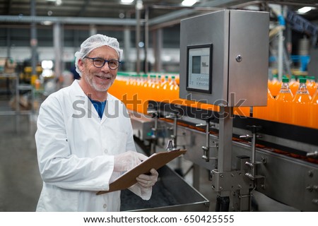 Portrait of smiling factory engineer maintaining record on clipboard in drinks production plant