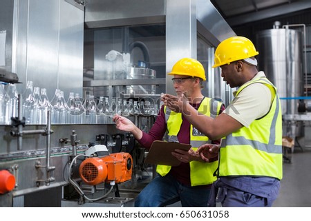 Two factory workers discussing while monitoring drinks production line at factory