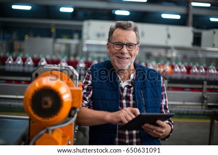 Portrait of smiling factory worker standing with a digital tablet in drinks production plant