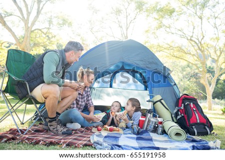 Family interacting while having snacks outside the tent at campsite