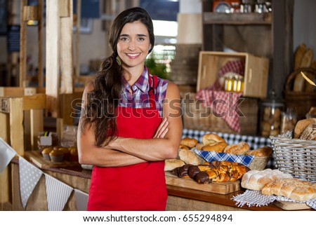 Portrait of smiling female staff standing with arms crossed at bakery shop in supermarket